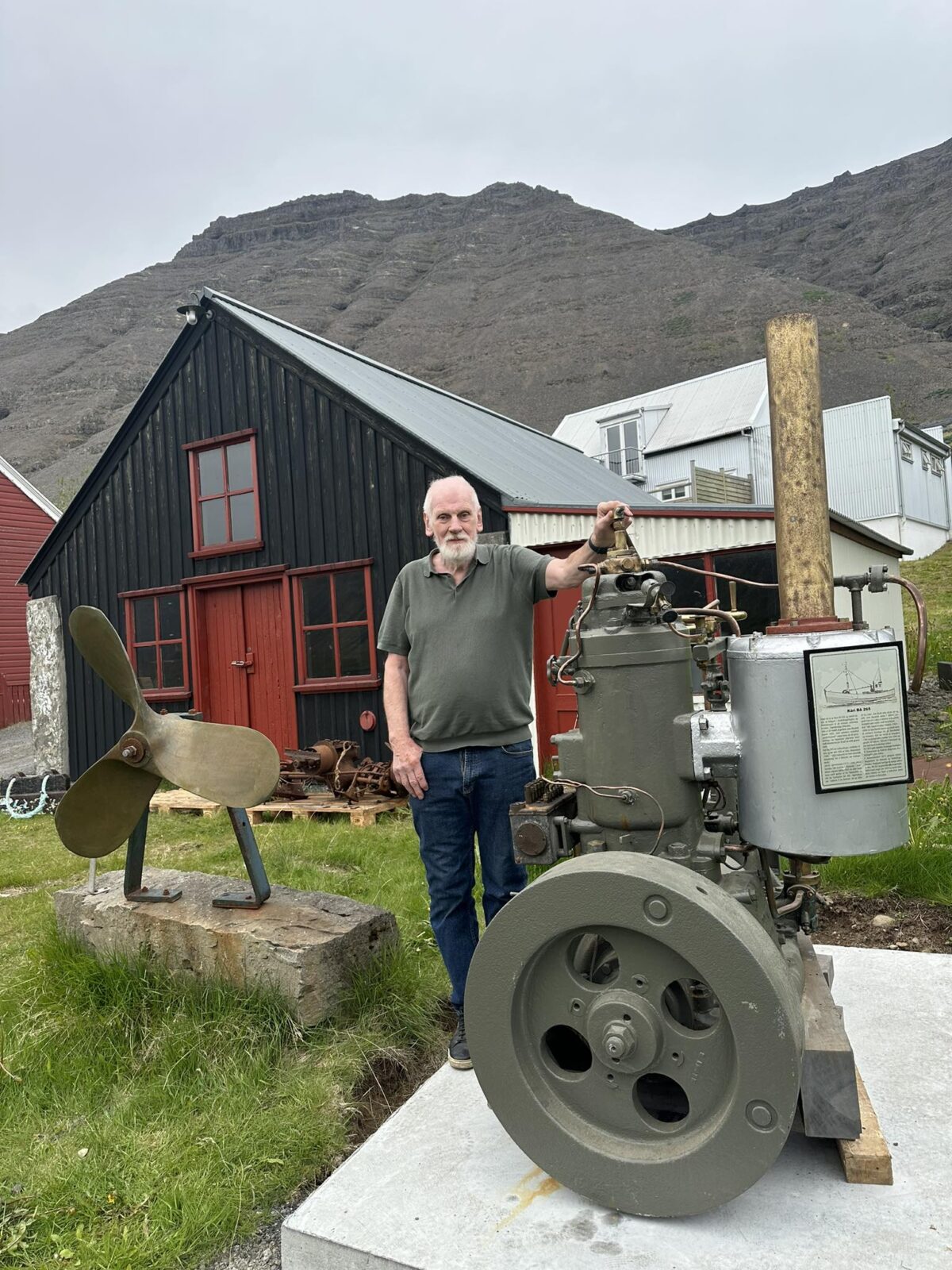 Jói Öddu fyrir framan Gömlu smiðjuna Til hægri er vélin úr Kára BA 265 sem Arnfirðingafélagið í Reykjavík gaf Vesturbyggð árið 2021.